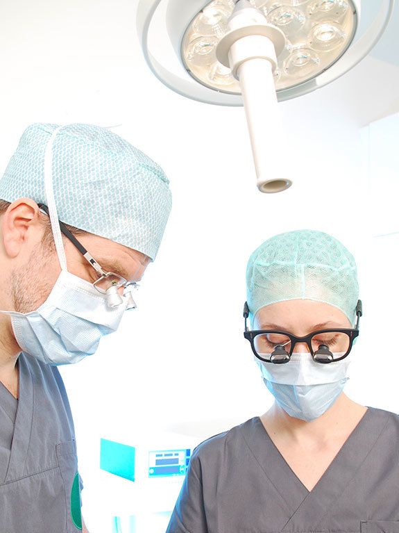 Dr. med. Juliane Finke und Dr. med. Stephan Frantzen arbeiten in OP-Kleidung, medizinischen Masken und chirurgischen Lupenbrillen im OP-Zimmer.