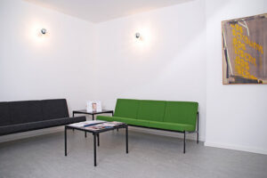 Wartebereich der Praxis mit zwei Sofas und Tischen mit Info-Material und Coffee Table Books.