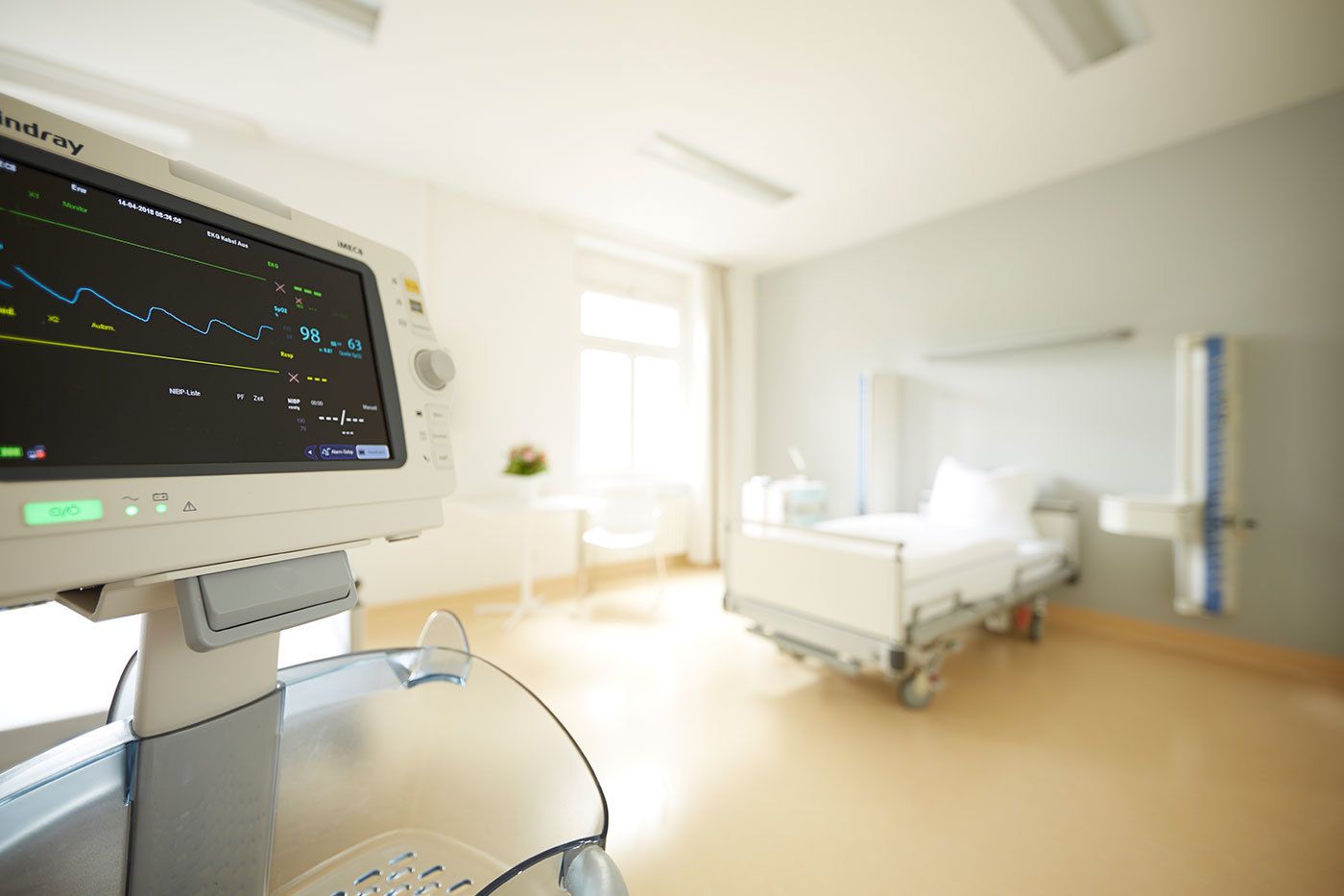 Das Patientzimmer ist hell und modern eingerichtet mit einem Krankenbett und technischen Geräten, die u.a. Vitalwerte anzeigen. Ein Tisch mit Stühlen lädt Gäste zum verweilen ein.