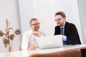 Dr. med. Mathias Reuteman und ein Patient sitzen vor einem MacBook und besprechen mögliche Prozeduren.