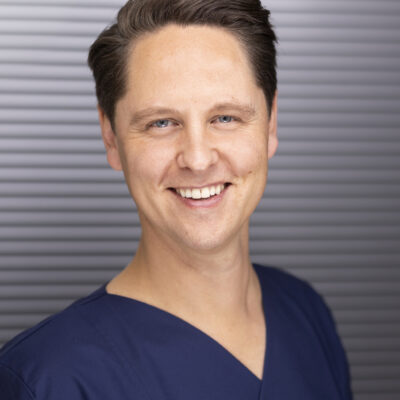Headshot von Dr. Frederic Hecker lächelnd. Aufgenommen vor einem dunklen Hintergrund.