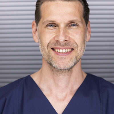 Headshot von Dr. Stefan Rösler lächelnd. Aufgenommen vor einem dunklen Hintergrund.