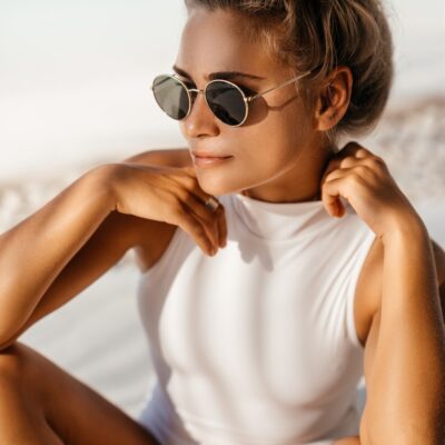 Eine junge Frau mit Sonnenbrille sitzt am Strand.