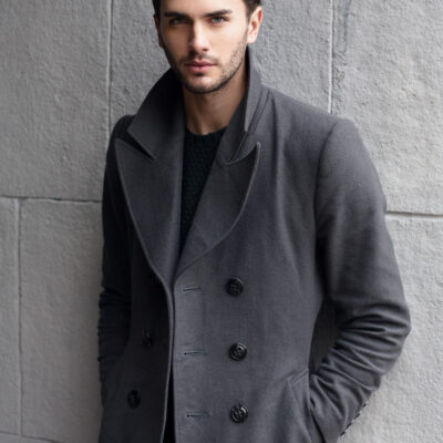 Ein Mann mit dichtem Haar trägt einen grauen Mantel.