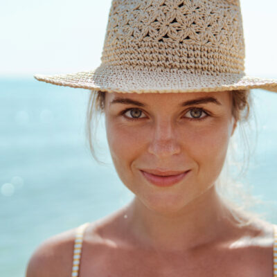 Woman radiates summer vibes wearing yellow striped bikini and a straw hat, enjoying her time on the beach.