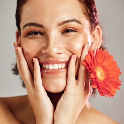 Lächelnde Frau mit Blume zwischen den Fingern hat eine natürliche Mimik nach einer Botox Behandlung.