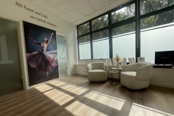 Heller, freundlicher Wartebereich der Schönheitsklinik mit modernen Sesseln, großen Fenster und einer künstlerischen Fotografie einer Ballerina. Die Botschaft 